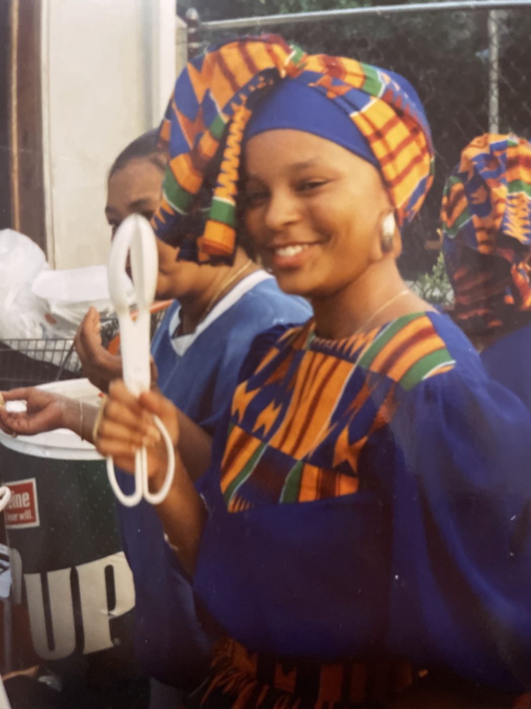Sonya smiling in kente cloth, holding scissors at a ribbon cutting